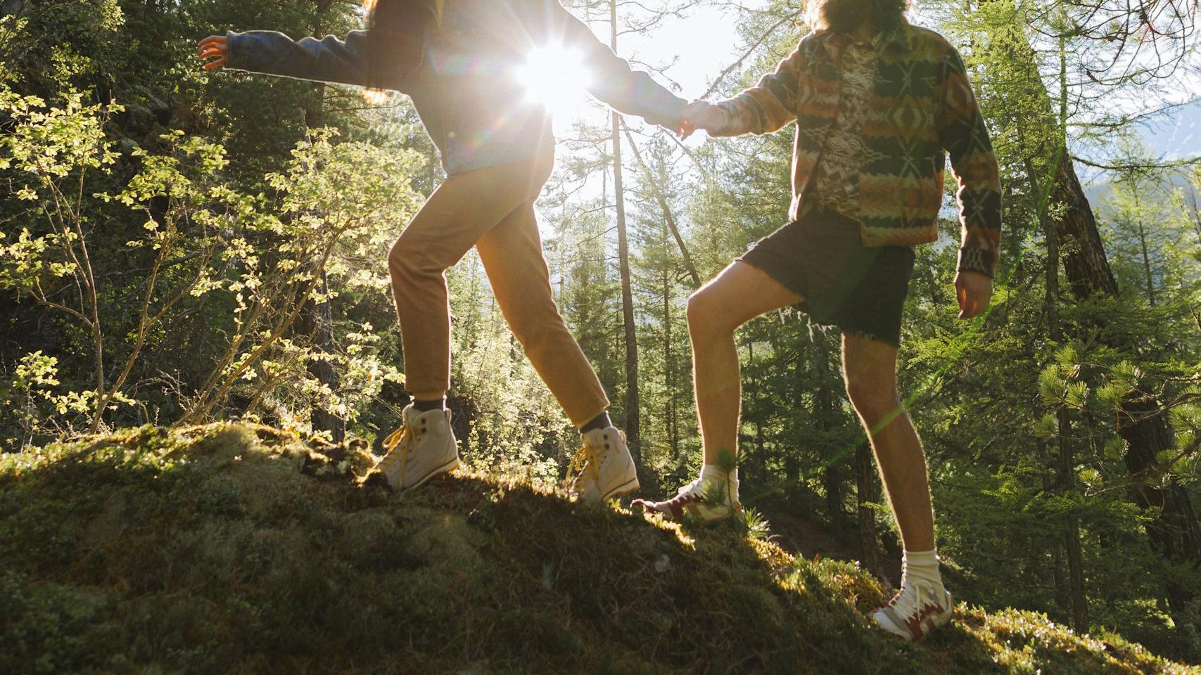 A couple hikes on a forest trail with sunlight streaming through trees.