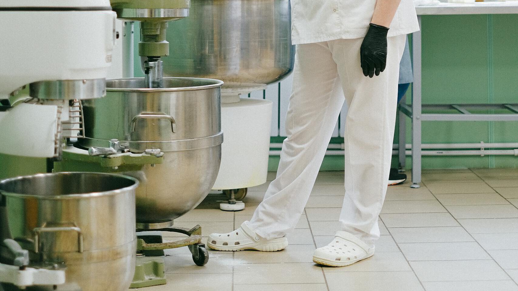 A food industry worker in a modern kitchen using an industrial mixer with protective gear.