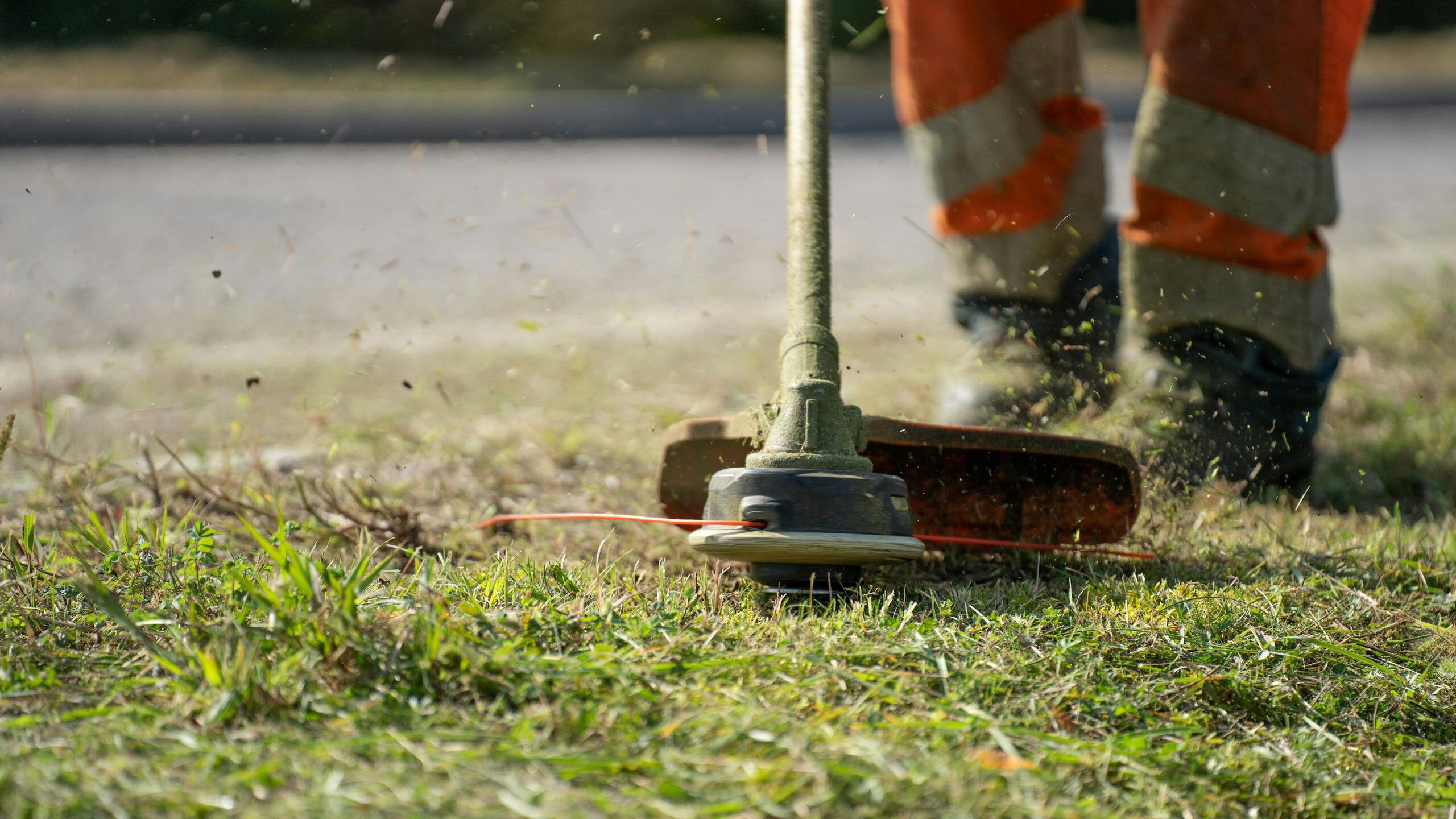 Close-up of a person trimming grass with a power tool outdoors.